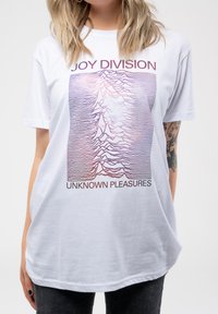 White cotton t-shirt featuring a graphic design of wavy lines in purple tones, with "JOY DIVISION" and "UNKNOWN PLEASURES" text below.