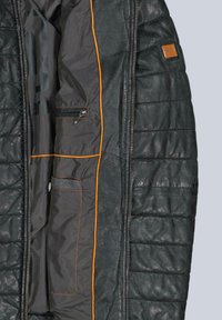 Schwarze gesteppte Jacke mit texturierter Außenseite, orangefarbener Innennaht, mehreren Taschen und einem Reißverschlussverschluss.