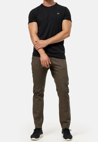 Zwart katoenen T-shirt met een ronde hals, korte mouwen en een klein wit logo. Gecombineerd met olijfgroene taps toelopende broek met kniezomen.