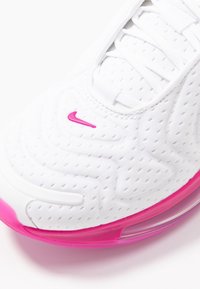 Basket de sport blanche avec un dessus texturé, dotée d'accents roses et d'une unité d'air visible dans la semelle. Les lacets sont blancs et plats.
