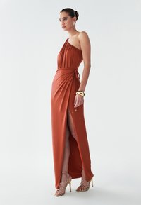 Maxi šaty v rezavé barvě s jedním ramínkem a bočním rozparkem, s nařasenými detaily na živůtku, zavazovací pas a zlaté sandály na podpatku.