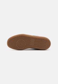 Semelle en caoutchouc marron avec des motifs circulaires et en vagues, présentant une finition texturée et des détails de marque près du talon.