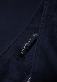 Tessuto blu navy con una superficie liscia presenta un'etichetta nera con la scritta "COMFORT" in bianco, cucita nel bordo.