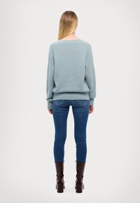 Hellblauer gestrickter Pullover mit lockerer Passform, gerippten Bündchen und Saum, kombiniert mit dunkelblauen Skinny Jeans und glänzenden braunen Stiefeletten.