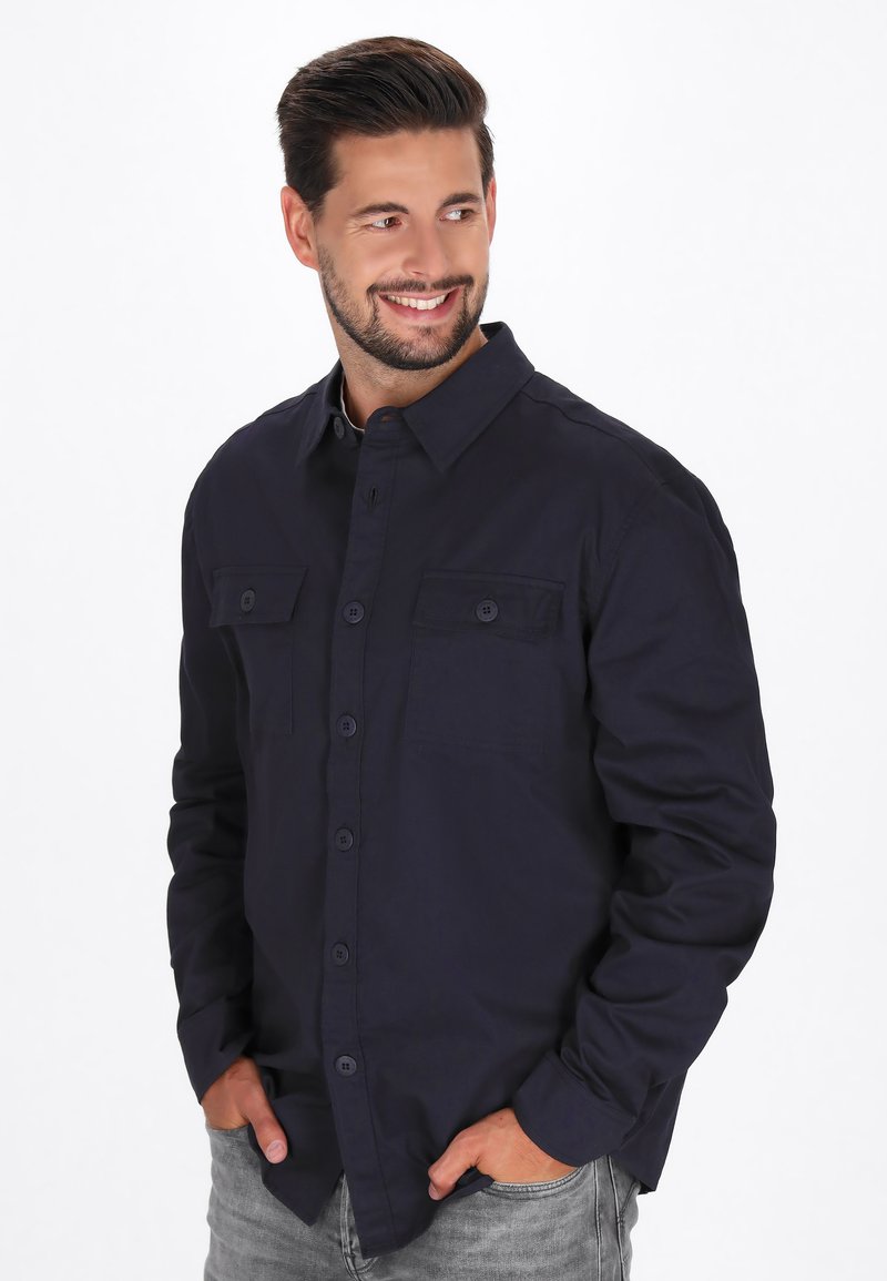 Camicia button-up blu scuro con maniche lunghe, due tasche sul petto e colletto classico. Il tessuto appare liscio e leggero.