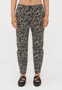 Pantaloni a fantasia neri e beige con un design affusolato e una cintura elastica, abbinati a scarpe nere flat. Presentano un dettaglio con bottone.