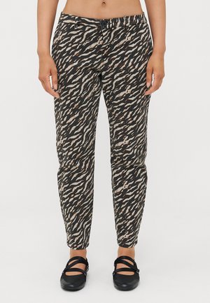 Pantalons à motifs noirs et beiges avec un design fuselé et une taille élastique, associés à des chaussures noires plates. Présente un détail de bouton.