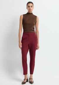 Bruine mouwloze coltrui met een gestructureerd patroon, gecombineerd met bordeaux geklede broek en bruine flats. Eenvoudige, aansluitende silhouet.