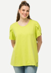 Limegrøn t-shirt lavet af blødt stof, med korte puffede ærmer, rund halsudskæring og sideskår ved kanten.