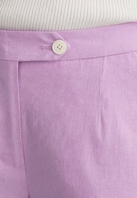 Levandulové lněné kalhoty s plochým předním dílem, zapínáním na jeden knoflík a jemnou texturou. Obsahují boční kapsy a pečlivě přežehlené záhyby.