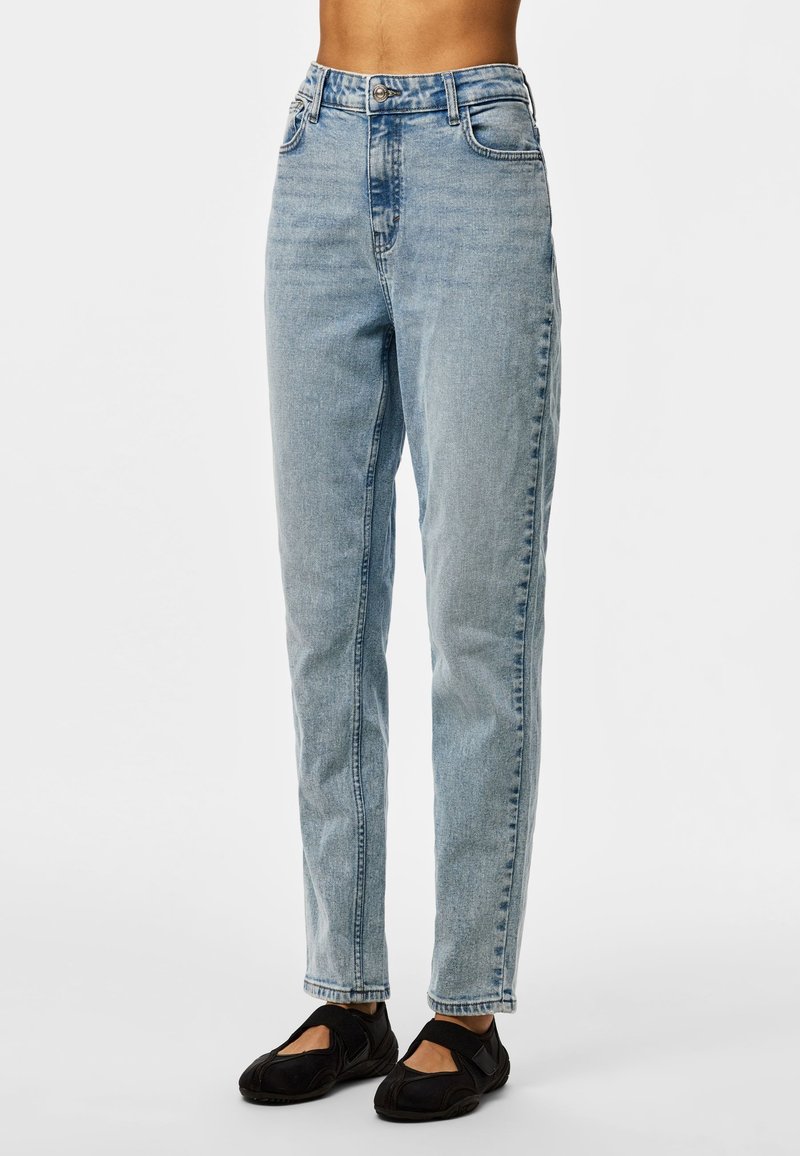 Light blue high-waist straight-leg jeans worn with black slip-on shoes, shown on a model standing against a plain background.