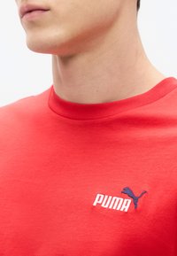 Κόκκινο βαμβακερό μπλουζάκι με στρογγυλή λαιμόκοψη, κοντά μανίκια και κεντημένο λευκό λογότυπο "PUMA" με σκιάλιο μπλε πάνθηρα.