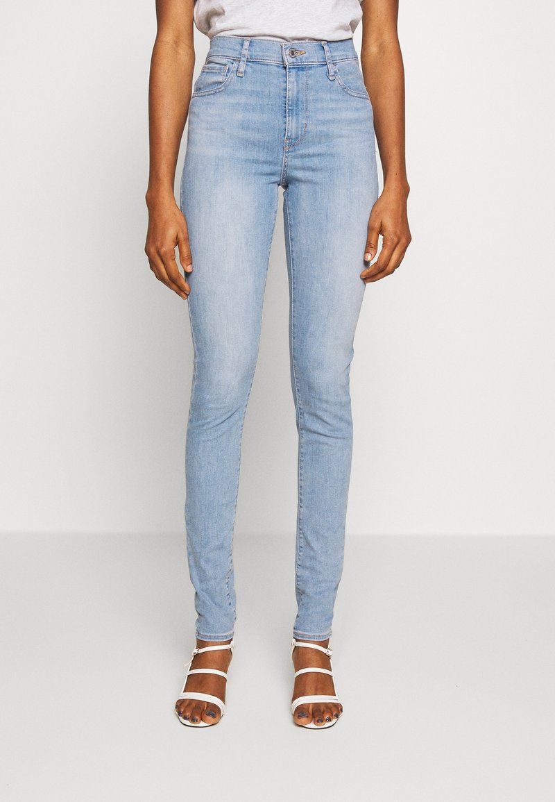 Jeans ajustados de color azul claro con una cintura alta y cinco bolsillos, que presentan una textura clásica de denim y un cierre de cremallera.