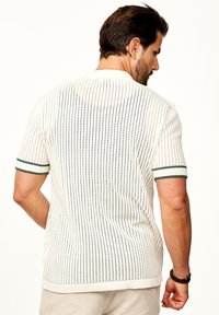 Weißer gestrickter Kurzarmpullover mit vertikalen Perforationen und grünen gerippten Akzenten an den Ärmeln. Die Rückansicht zeigt die Gesamtstruktur.