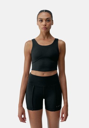 Svart atletisk crop-top med rund halsringning og tætsiddende design, parret med højttlivede sorte shorts med subtile sømme og accenter.