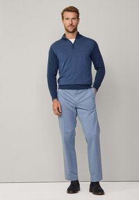 Maglione a collo zip blu navy con motivo testurizzato, abbinato a pantaloni azzurri chiari e scarpe scure. Design semplice e aderente.