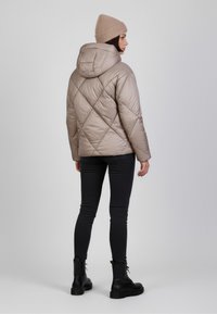 Giacca in puffer beige con cappuccio, caratterizzata da cuciture a rombi. Abbinata a pantaloni neri skinny e stivaletti neri con lacci. Berretto lavorato a maglia in tonalità neutra.