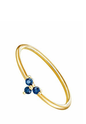 Anillo delgado de oro con tres pequeñas piedras preciosas redondas azules dispuestas en un grupo triangular sobre un fondo blanco.