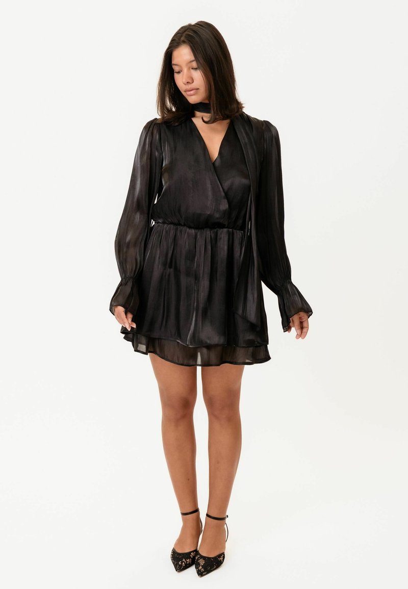 Rochie mini neagră, plisată, cu mâneci lungi și decolteu adânc în V. Material transparent cu un luciu delicat; prezintă un guler legat și o fustă fluidă.