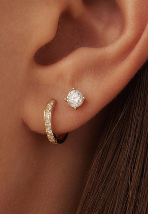 Boucles d'oreilles en or avec des créoles et des studs, mettant en avant une pierre précieuse ronde et claire entourée de six griffes, et une petite créole ornée de plusieurs petites pierres claires.