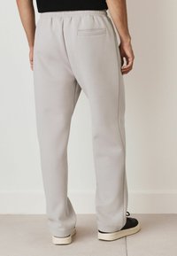 Light grey sweatpants made of soft fabric, featuring an elastic waistband, a back pocket, and tapered cuffs at the ankle.