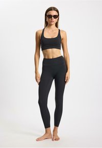 Zwart sportset bestaande uit een cropped tanktop en een legging met hoge taille. De stof is glad met een aansluitend ontwerp en minimale naden.