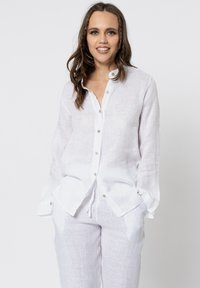 Camicia bianca in lino con maniche lunghe, parte anteriore con bottoni e due tasche laterali. Tessuto leggero e texturizzato con una vestibilità morbida.