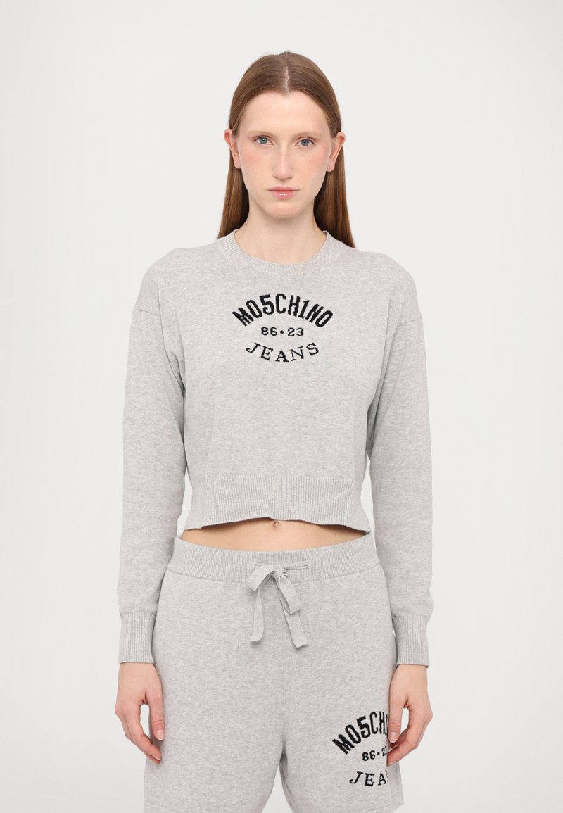 Sweatshirt cinzento cortado com punhos canelados, apresentando texto gráfico preto "MOSCHINO JEANS 86-23" no peito, combinado com calças de moletom a condizer.