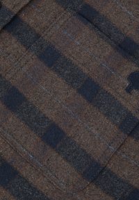 Bruin en marineblauw geruite wollen stof met een zachte textuur, voorzien van blauwe stiksels en een klein logo in de hoek.