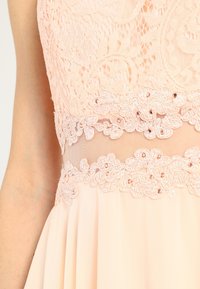 Robe sans manches rose pâle avec corsage en dentelle et taille en dentelle florale ornée de petites perles, jupe fluide en chiffon.