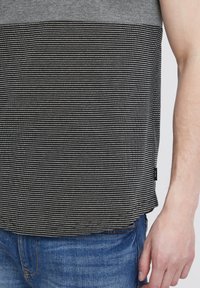 Camiseta de manga corta con un patrón a rayas en negro y gris, hecha de algodón, con un dobladillo recto y una pequeña etiqueta en el costado.