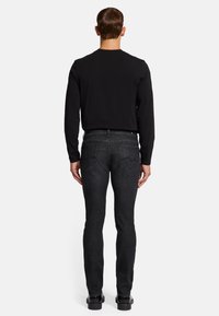 Chemise noire ajustée à manches longues associée à un jean en denim gris foncé, avec une texture douce et des poches arrière agrémentées de coutures discrètes.