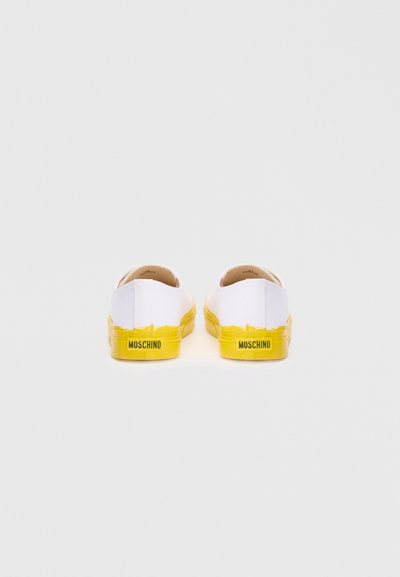 White canvas sneakers with yellow rubber soles and accents. The back features the brand name "Moschino" in black. Simple, low-profile design.
