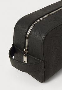 Black textured leather toiletry bag with silver zipper closed and side handle on plain white background.