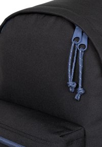 Černý látkový batoh s zaobleným vrškem, vybavený modrými stahovacími šňůrkami a texturovaným povrchem. Zipy jsou výrazné na vrchu.