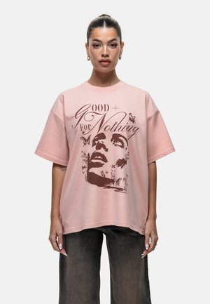 Roze oversized t-shirt met korte mouwen, voorzien van een grafische print van een gezicht en vlinders in bruintinten. Zacht katoen, relaxte pasvorm.