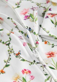 Tessuto bianco con stampe floreali e farfalle colorate, dotato di una cerniera in plastica bianca al centro.