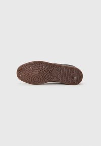 Svart sneaker såle med intrikat mønster, med en sirkulær logo på hælen og brunt gummimateriale for grep.
