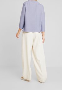 Ljuslila stickad topp med trekvartslånga ärmar och ribbad textur. Matchas med löst sittande, krämfärgade byxor för en avslappnad look.