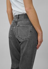 Gray denim jeans with a high waist, featuring two back pockets and a leather patch near the waistband. The fabric has a textured finish.