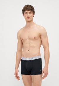 Μαύρα μποξεράκια από ελαστικό ύφασμα, με ζώνη στη μέση σε γκρι χρώμα με το λογότυπο της Nike και σχέδιο που αγκαλιάζει το σώμα.