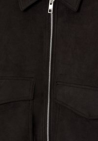 Giacca in suede nera con chiusura frontale a zip, colletto appuntito e due tasche sul petto. Texture liscia con sottili dettagli di cucitura.
