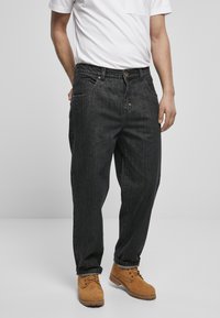 Sorte denim jeans med en afslappet pasform, der har frontlommer, knaplukning og diskret slid. Parret med brune arbejdsstøvler.