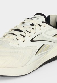 Λευκό και μαύρο αθλητικό παπούτσι Reebok με υφασμάτινη υφή, κορδόνια και λογότυπο στο πλάι και στη γλώσσα, σε κοντινή μπροστινή γωνία.