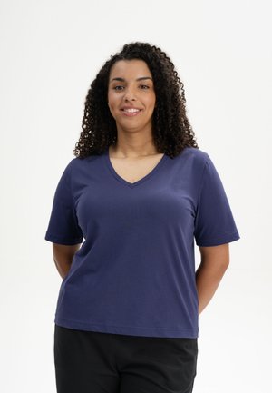 Marineblaues kurzärmliges V-Ausschnitt-T-Shirt aus weichem Baumwollmaterial, mit lockerer Passform und geradem Saum, getragen mit schwarzen Hosen.