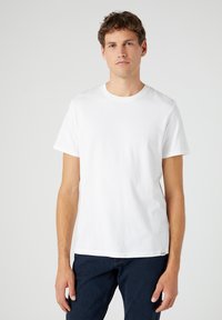 T-shirt in cotone bianco con colletto rotondo e maniche corte. Orlo dritto e una piccola etichetta del marchio sul lato inferiore. Tessuto semplice.