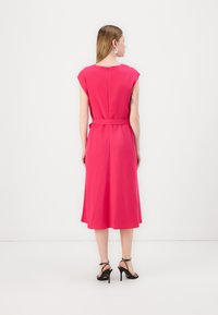 Rózsaszín ujjatlan ruha, amelynek szűk derékrésze és bővülő szoknyája van, kulcslyuk hátkivágással. Fekete magassarkú szandálokkal viselve.