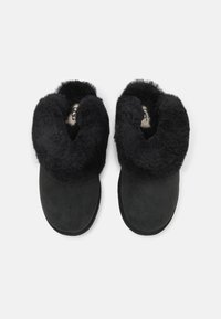 Chaussons en peau de mouton noir avec un col en peluche et un extérieur en daim, dotés d'un bout rond et d'une semelle plate.