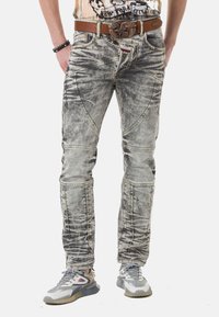 Ausgebleichte graue Jeans aus Denim mit einzigartiger Nahtführung, präsentiert mit einem braunen Gürtel und grauen Sneakers. Abgenutzte Textur und schmaler Schnitt.