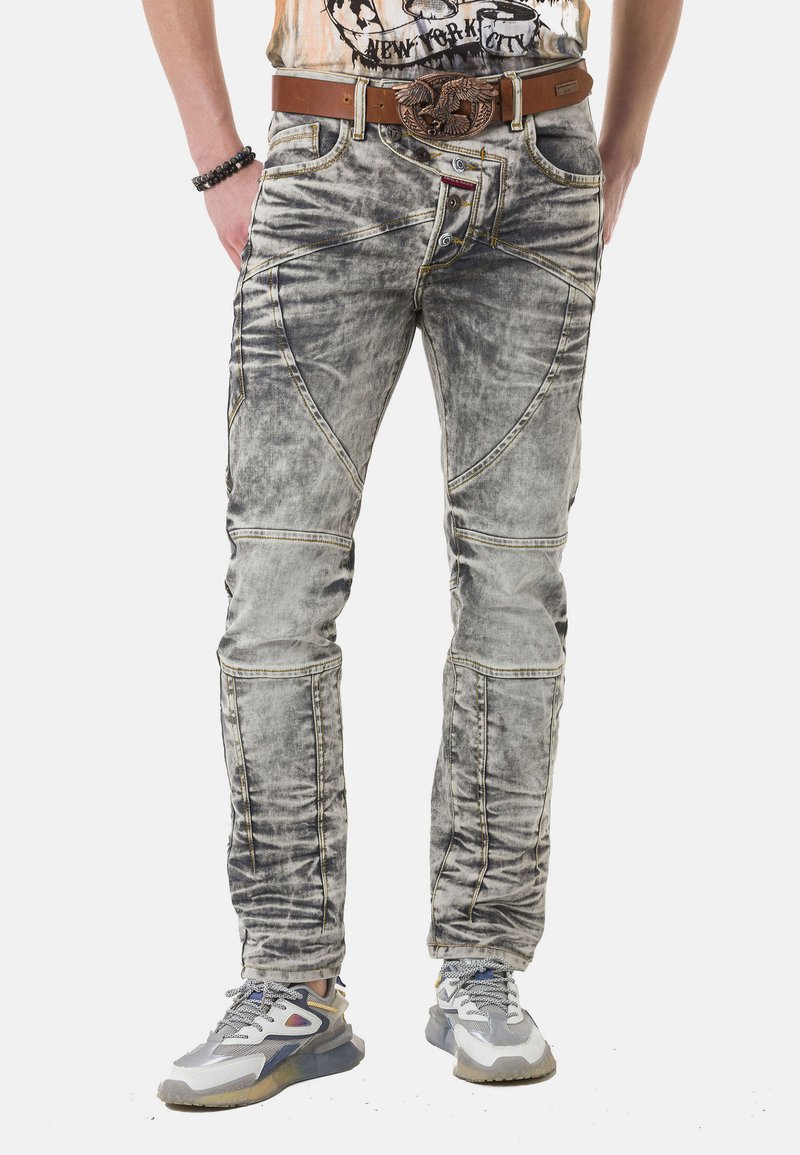 Ausgebleichte graue Jeans aus Denim mit einzigartiger Nahtführung, präsentiert mit einem braunen Gürtel und grauen Sneakers. Abgenutzte Textur und schmaler Schnitt.